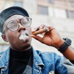 close-up-portrait-african-american-man-jeans-jacket-beret-eyeglasses-smoking-cigar